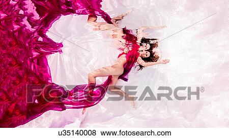 Stock Photo - Underwater view of woman draped in sheer fabric, floating towards water surface. Fotosearch