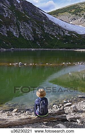 Stock Image - USA, Colorado, Idaho Springs, Hiker sitting by lake below Saint Mary's Glacier. Fotosearch