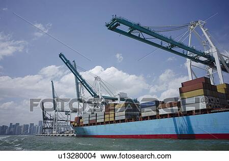 Picture - USA, Florida, Miami, Container ship with cranes and city skyline in background. Fotosearch