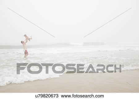 Stock Image - USA, New York, Monatuk, Father and daughter (2-3) on beach by ocean. Fotosearch