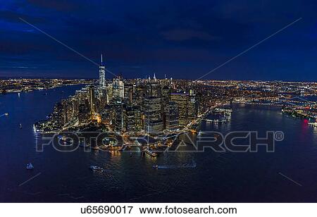 Stock Photo - USA, New York, New York City, Manhattan, Aerial view of illuminated skyline with harbor at night. Fotosearch