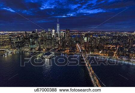 Stock Photo - USA, New York, New York City, Manhattan, Aerial view of illuminated skyline with harbor and Brooklyn bridge at night. Fotosearch