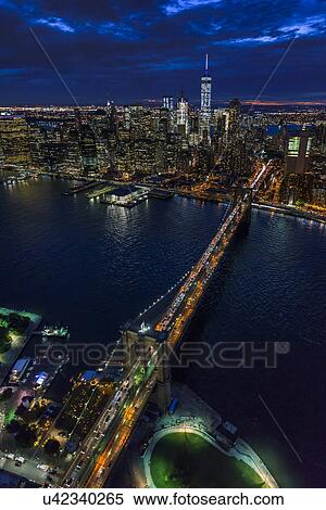 Stock Photography - USA, New York, New York City, Manhattan, Aerial view of illuminated skyline with harbor and Brooklyn bridge at night. Fotosearch