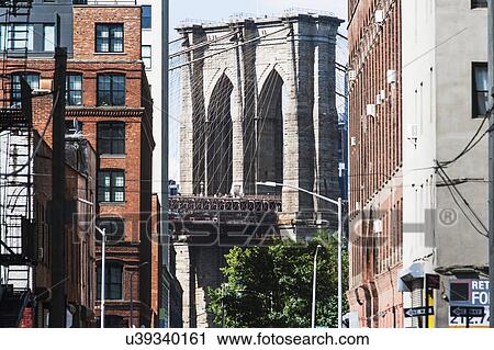 Stock Image - USA, New York State, New York City, Brooklyn Bridge arches seen from between buildings. Fotosearch