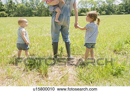 Stock Image - USA, Pennsylvania, Washington Crossing, Mother with three daughters (18-23 months, 2-3) walking on green field. Fotosearch