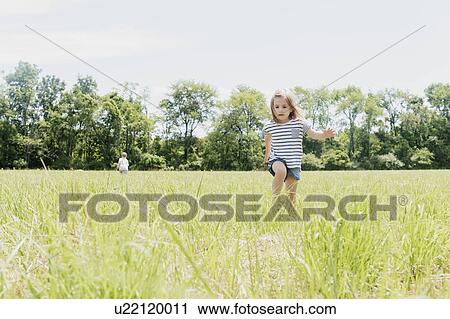 Stock Image - USA, Pennsylvania, Washington Crossing, Girl (2-3) and boy (4-5) walking on green field. Fotosearch