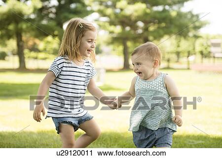 Stock Image - USA, Pennsylvania, Washington Crossing, Two sisters (18-23 months, 2-3) holding hands and walking together. Fotosearch