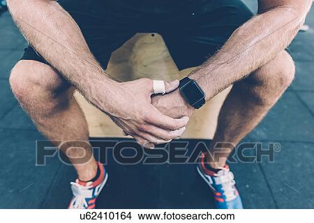Picture - Waist down view of male cross trainer sitting on box in gym. Fotosearch