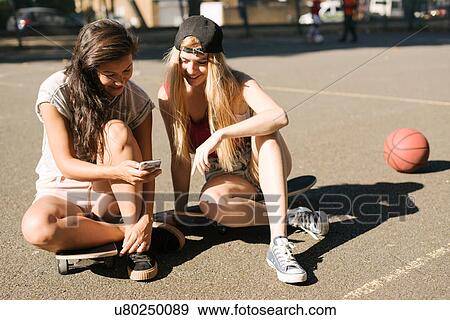 Stock Photo - Woman and friend reading smartphone update on basketball court. Fotosearch