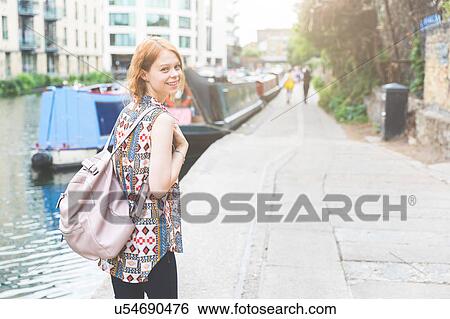 Woman by canal looking over shoulder at camera smiling, London, UK View Large Photo Image Stock Photograph - Woman by canal looking over shoulder at camera smiling, London, UK. Fotosearch