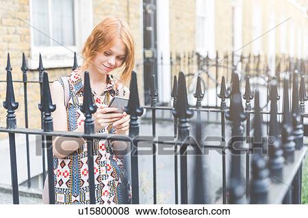 Stock Photo - Woman by house texting on smartphone, London, UK. Fotosearch