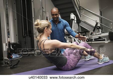 Stock Image - Woman exercising with personal trainer in gym. Fotosearch