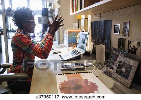 Stock Photo - Woman gesturing in front of laptop in office. Fotosearch