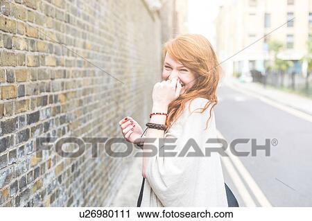 Stock Image - Woman, hand on mouth looking at camera smiling, London, UK. Fotosearch