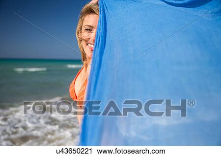 Stock Image - Woman holding up scarf on beach. Fotosearch