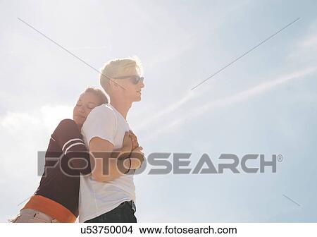 Picture - Woman hugging boyfriend against sunlit blue sky. Fotosearch