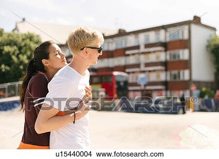 Picture - Woman hugging boyfriend in city skatepark. Fotosearch