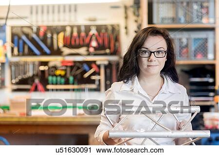Stock Image - Woman in bicycle repair shop holding bicycle part. Fotosearch