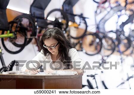 Stock Image - Woman in bicycle shop working at counter. Fotosearch