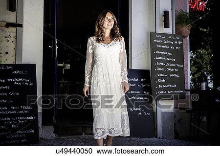 Stock Image - Woman in cafe doorway looking away smiling, Berlin, Germany. Fotosearch