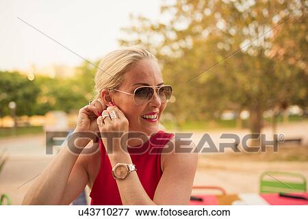 Stock Photo - Woman in red putting in earring at park, Alicante, Spain. Fotosearch