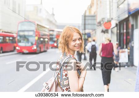 Picture - Woman in street looking over shoulder at camera smiling, London, UK. Fotosearch