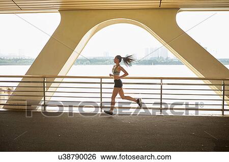 Stock Photograph - Woman jogging on elevated walkway, South Bund, Shanghai, China. Fotosearch