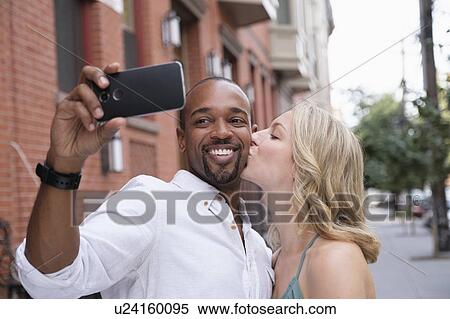 Woman kissing boyfriend in cheek, man taking selfie View Large Photo Image Stock Photography - Woman kissing boyfriend in cheek, man taking selfie. Fotosearch