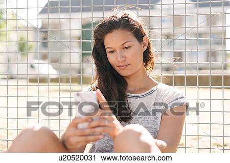 Woman reading smartphone updates by wire fence View Large Photo Image Stock Image - Woman reading smartphone updates by wire fence. Fotosearch