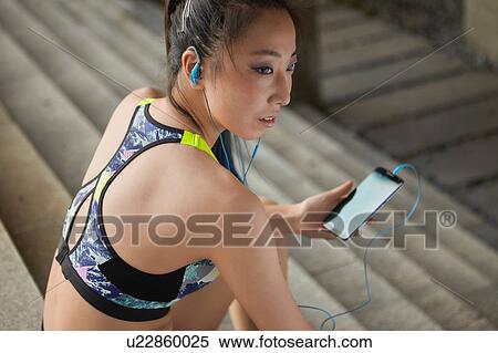 Stock Photography - Woman sitting on steps wearing earphones holding smartphone. Fotosearch