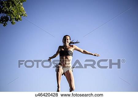 Stock Photo - Woman wearing bikini jumping in mid air. Fotosearch