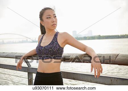 Stock Image - Woman wearing crop top by river looking away, South Bund, Shanghai, China. Fotosearch