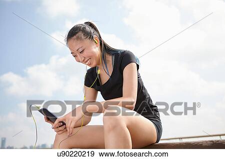 Woman wearing earphones holding smartphone smiling View Large Photo Image Stock Photo - Woman wearing earphones holding smartphone smiling. Fotosearch