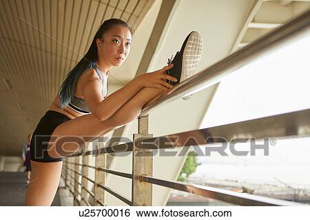 Stock Photograph - Woman with leg raised on railing stretching. Fotosearch