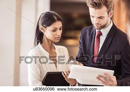 Young businessman and woman reading paperwork in office View Large Photo Image Stock Photograph - Young businessman and woman reading paperwork in office. Fotosearch