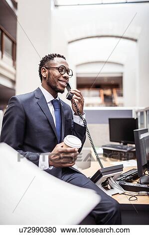 Stock Image - Young businessman talking on landline telephone in office. Fotosearch