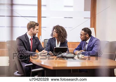 Stock Photo - Young businesswoman and two businessmen brainstorming at boardroom table. Fotosearch