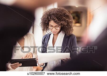 Stock Photo - Young businesswoman reading paperwork in office. Fotosearch