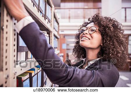 Stock Photograph - Young businesswoman searching office shelves. Fotosearch