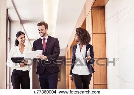 Young businesswomen and businessman walking and reading paperwork in office corridor View Large Photo Image Picture - Young businesswomen and businessman walking and reading paperwork in office corridor. Fotosearch