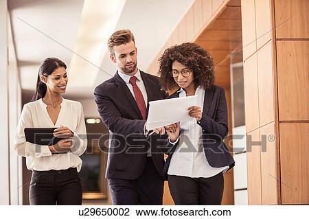 Young businesswomen and businessman walking and reading paperwork in office corridor View Large Photo Image Stock Image - Young businesswomen and businessman walking and reading paperwork in office corridor. Fotosearch