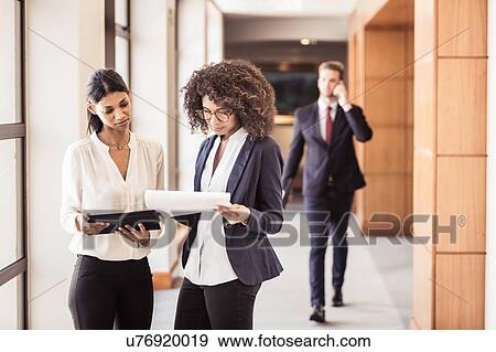 Stock Photo - Young businesswomen reading paperwork in office corridor. Fotosearch