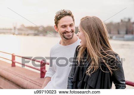 Young couple chatting on waterfront at sunset, Battersea Park, London, UK View Large Photo Image Stock Image - Young couple chatting on waterfront at sunset, Battersea Park, London, UK. Fotosearch