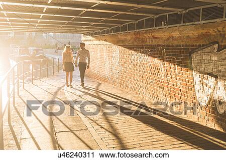 Stock Image - Young couple strolling under bridge on Regent's Canal, London, UK. Fotosearch