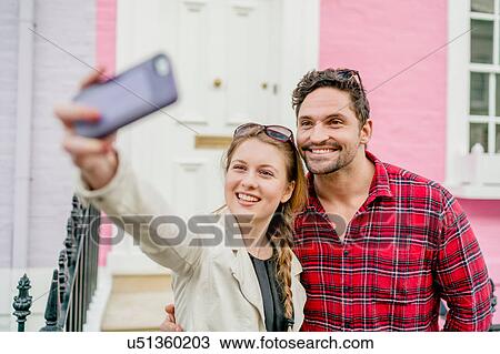 Stock Image - Young couple taking selfie in front of pink house, Kings Road, London, UK. Fotosearch