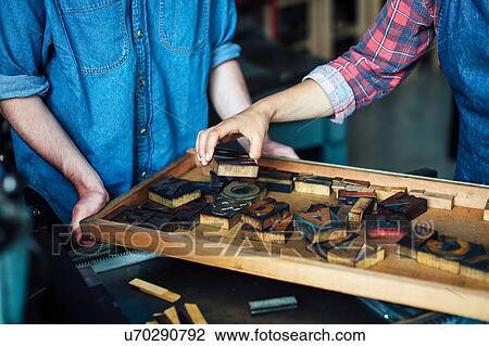 Stock Image - Young craftsman and craftswoman looking at letters in letterpress studio, mid section. Fotosearch