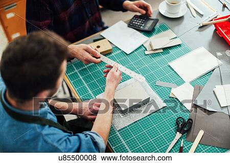 Stock Photo - Young craftsman passing metal ruler to friend in print studio, elevated view. Fotosearch