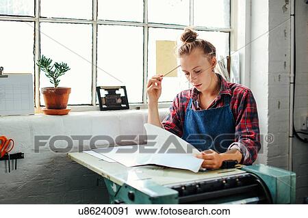 Young craftswoman by window, leaning on letterpress machinery and looking at paperwork in book arts studio View Large Photo Image Stock Image - Young craftswoman by window, leaning on letterpress machinery and looking at paperwork in book arts studio. Fotosearch