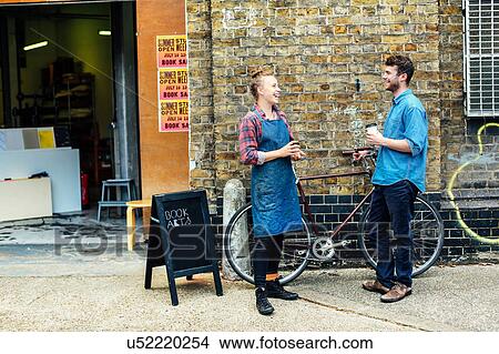 Picture - Young craftswoman outside workshop, laughing and chatting to young man with push bike. Fotosearch
