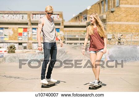 Stock Photo - Young female and male skateboarding friends skateboarding in skatepark. Fotosearch